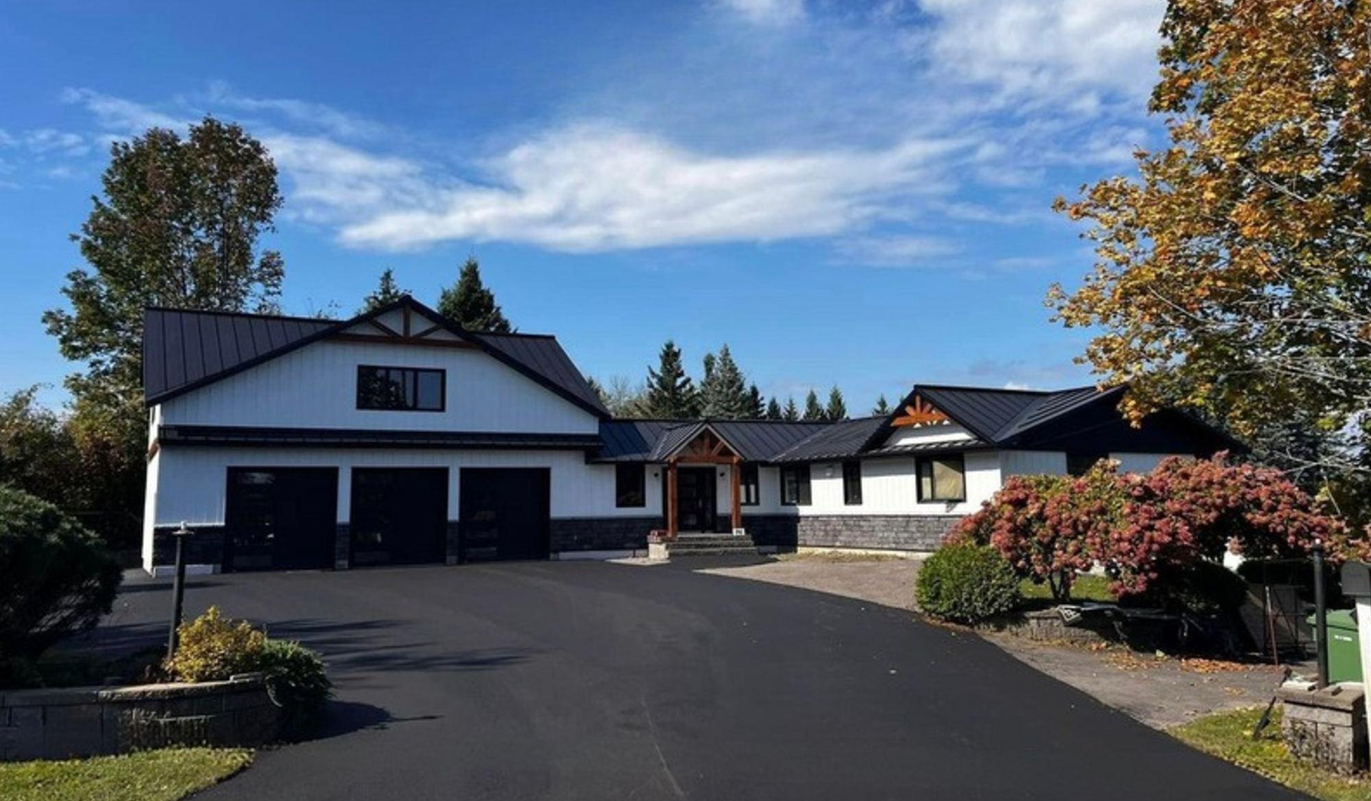 Garage triple intégré à une maison au revêtement blanc et à la toiture métallique noire